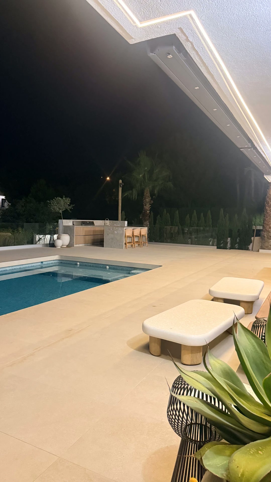 Illuminated pool terrace at night with outdoor kitchen and designer seating